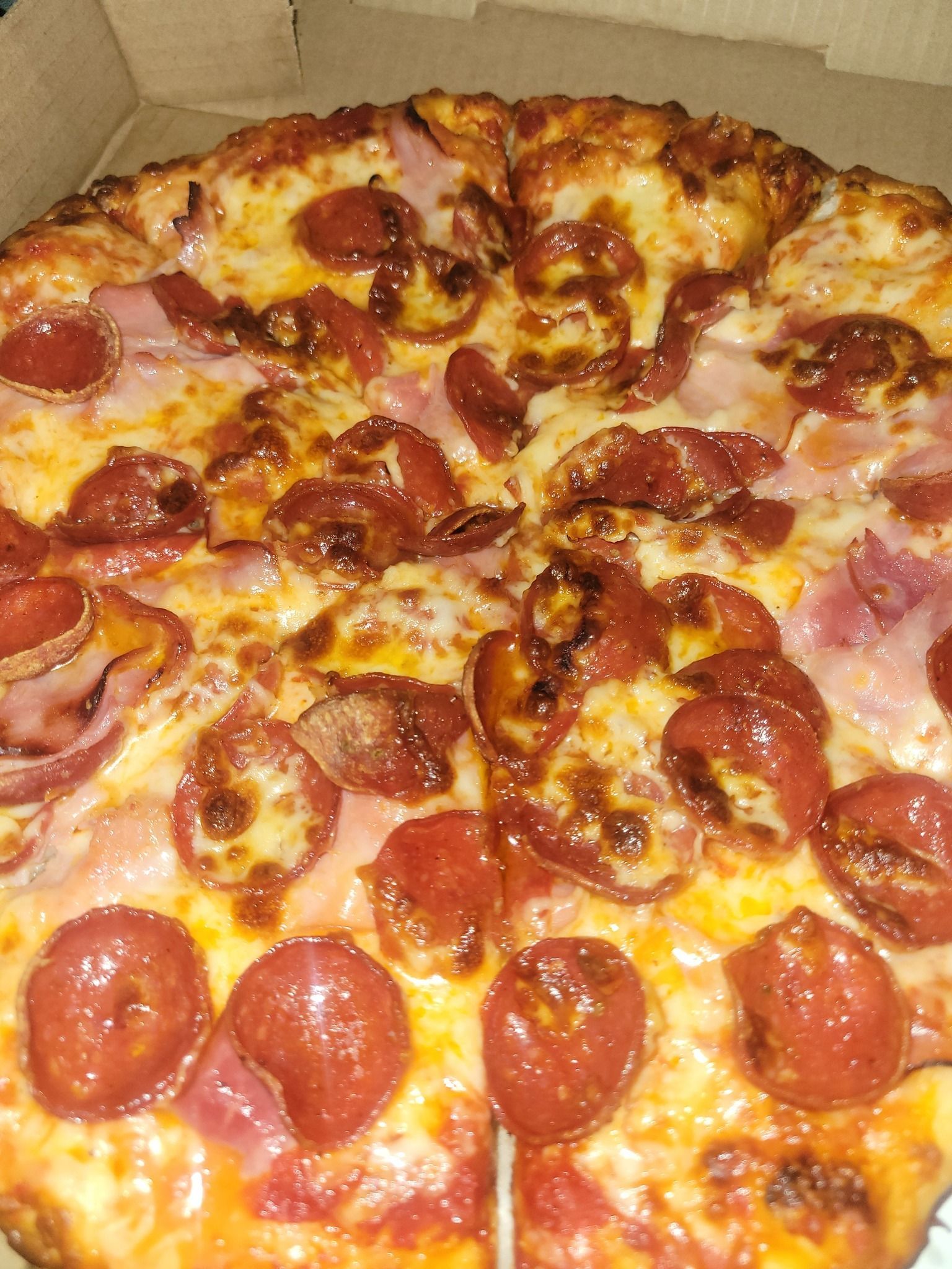 Pepperoni pizza with ham and melted cheese on a cardboard box