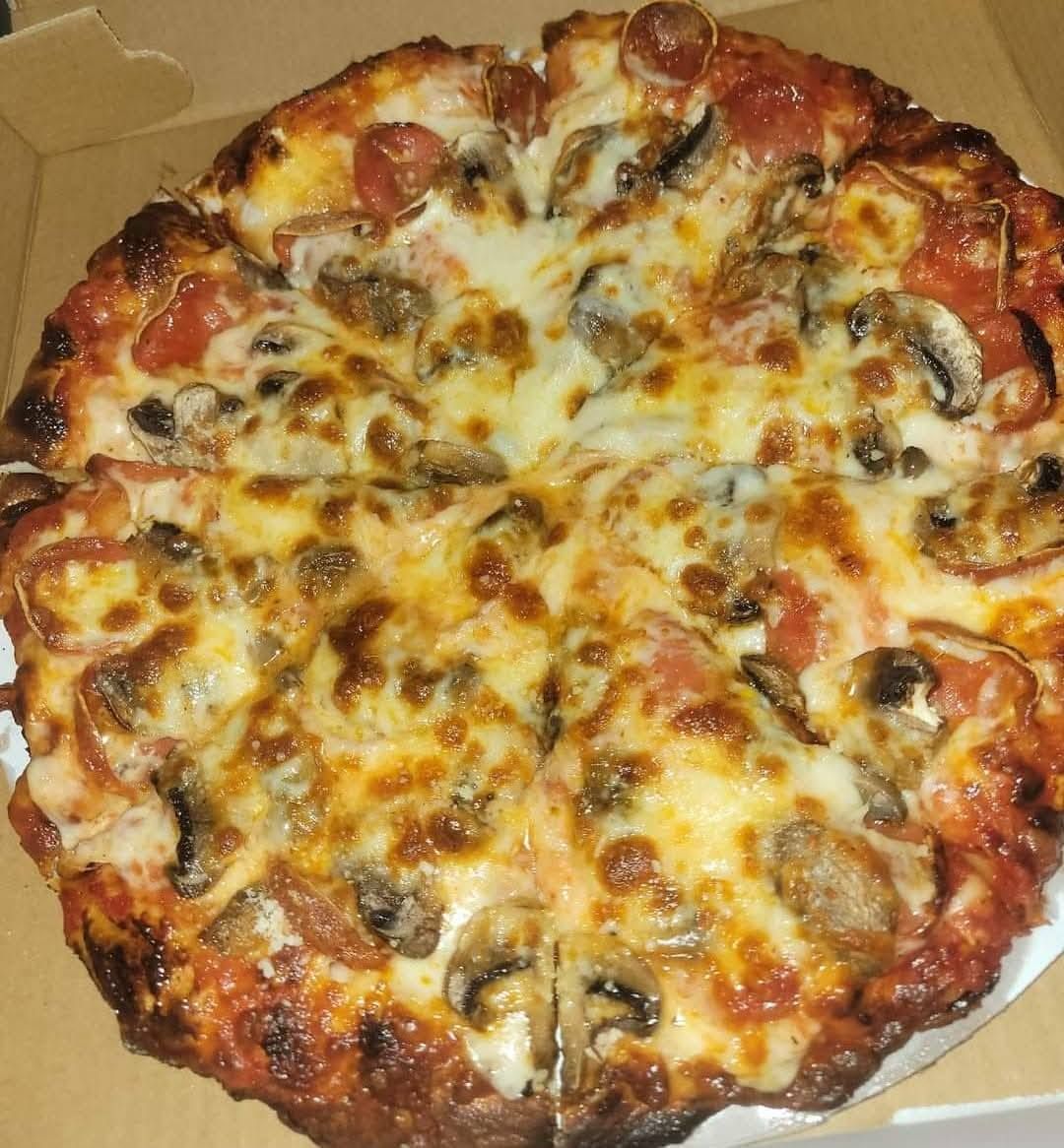 Pepperoni and mushroom pizza in a cardboard box, topped with melted cheese and tomato sauce