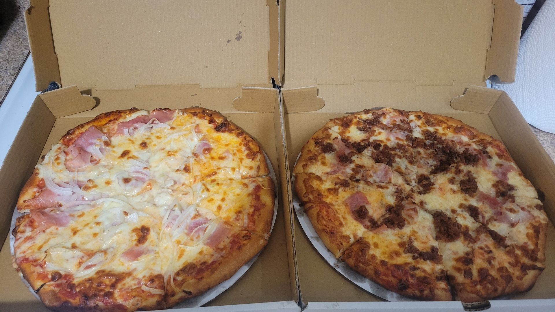 Two pizzas in open boxes, one cheese and one browned meat topping, on a table.