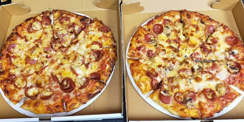 Two pepperoni pizzas in open cardboard boxes side by side
