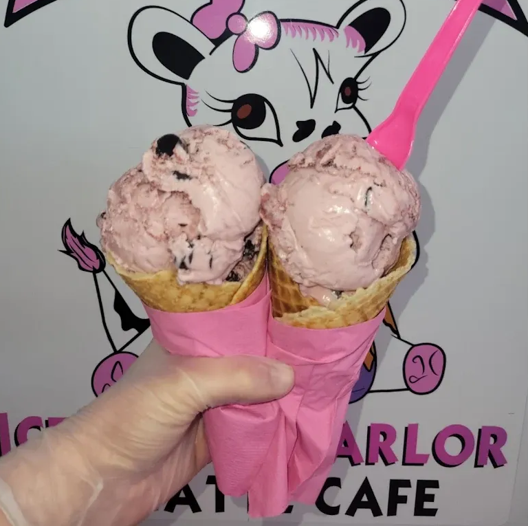 Hand holding two pink ice cream cones in front of a cartoon cat cafe sign