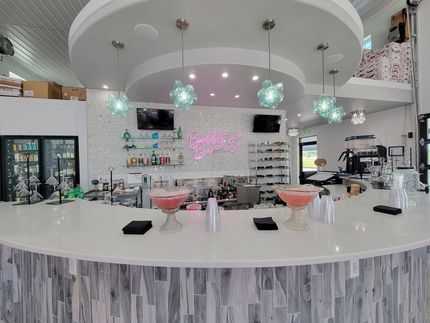 Bright modern bar with white curved counter, hanging lights, and glass shelves behind it