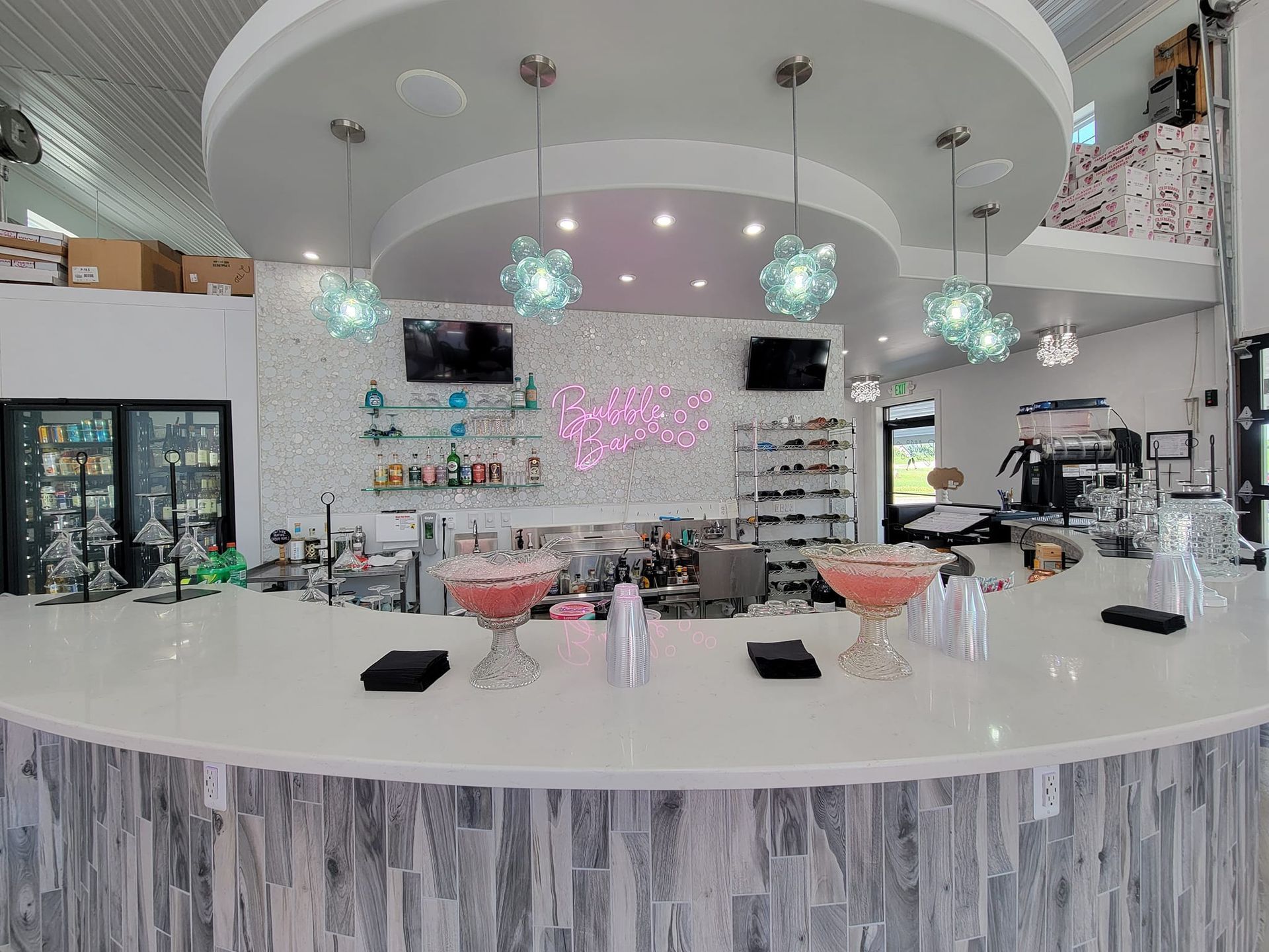 Modern café interior with a white curved counter, hanging lights, and display fridges in the background