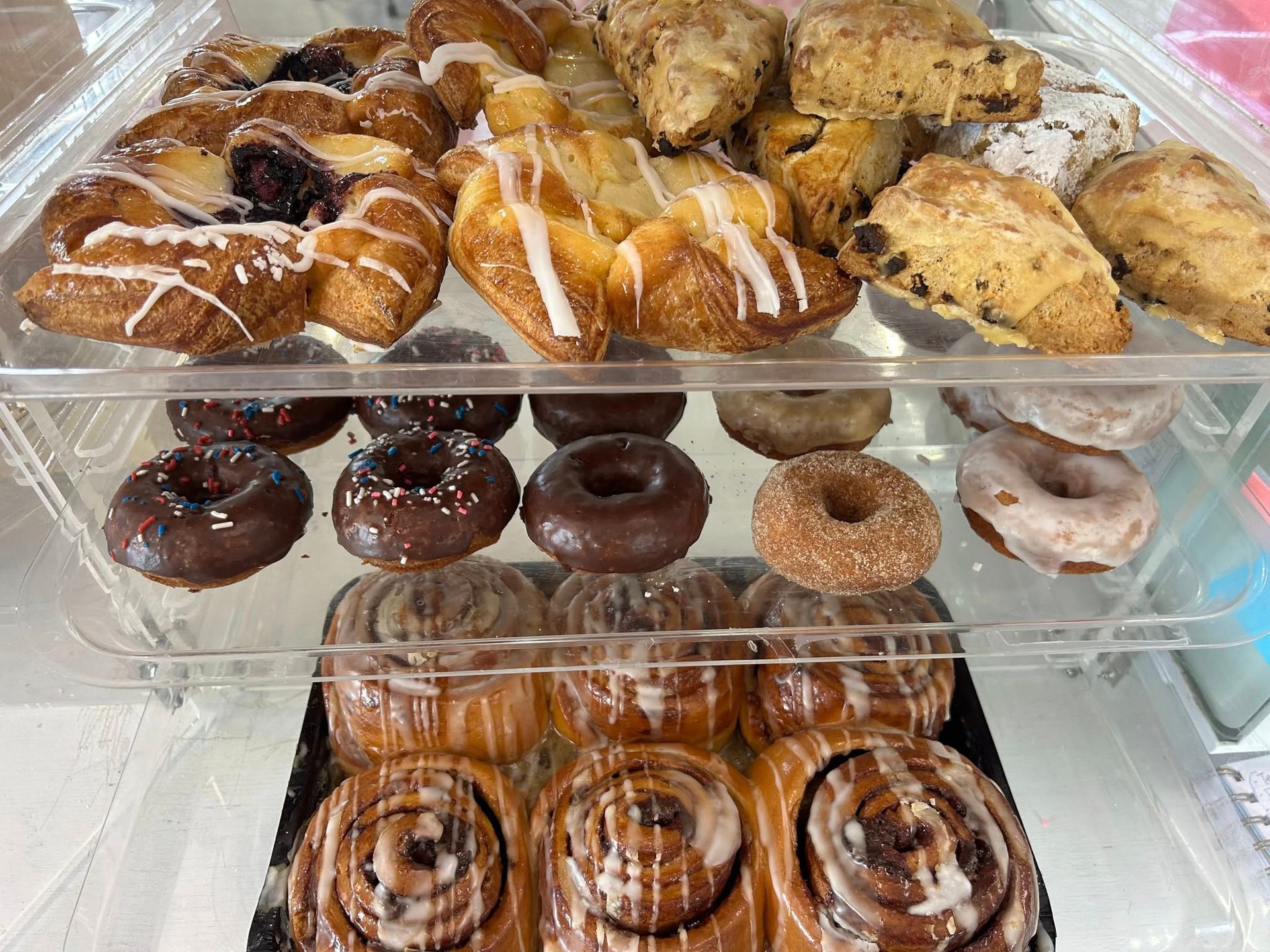 Assorted pastries and donuts displayed in a clear plastic bakery case.