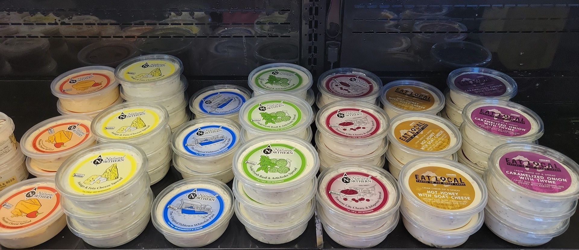 Stacked tubs of colorful ice cream or frozen dessert with labeled lids in a freezer display.