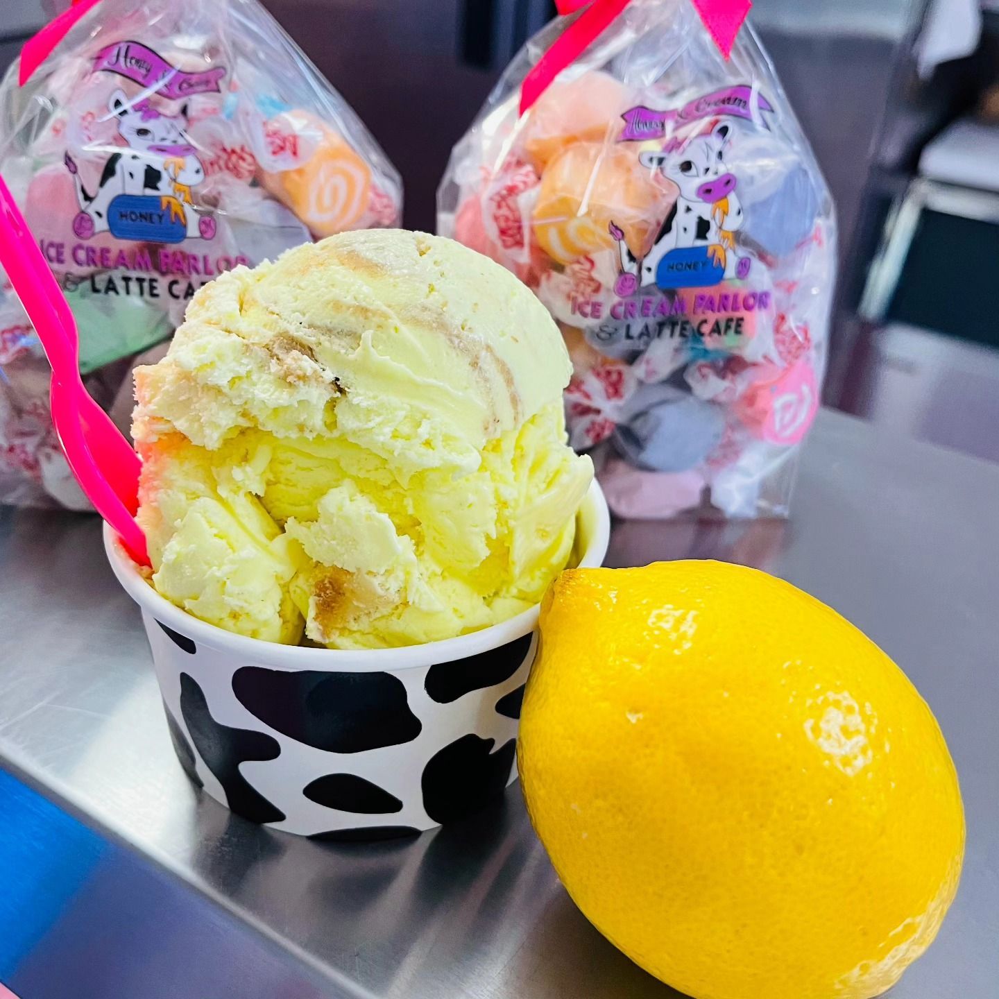 Yellow ice cream in a black-and-white cup beside a lemon, with packaged treats in the background