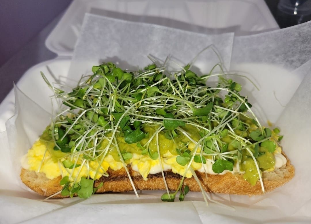 Open sandwich topped with avocado, scrambled egg, and microgreens on white paper