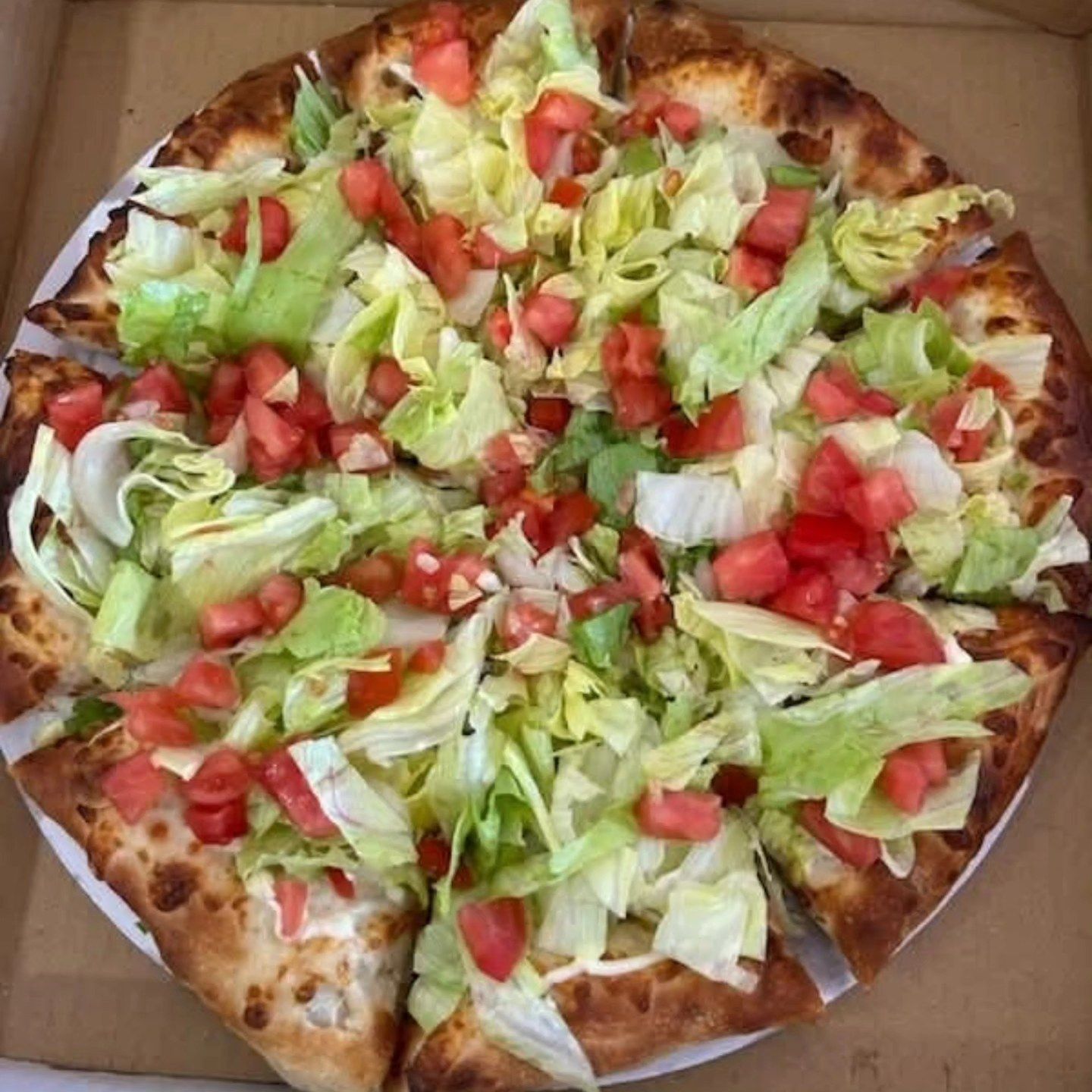 A large pizza topped with lettuce, diced tomatoes, and onions in an open box.