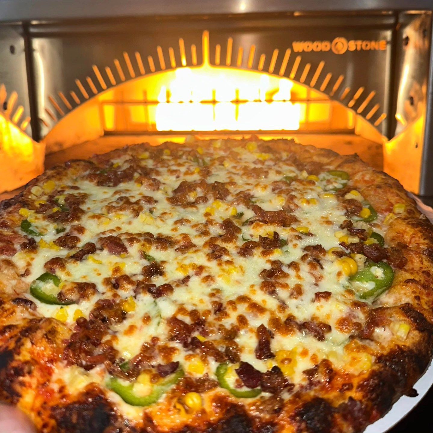 Cheesy pizza baking in a wood-fired oven with a browned crust and visible green peppers