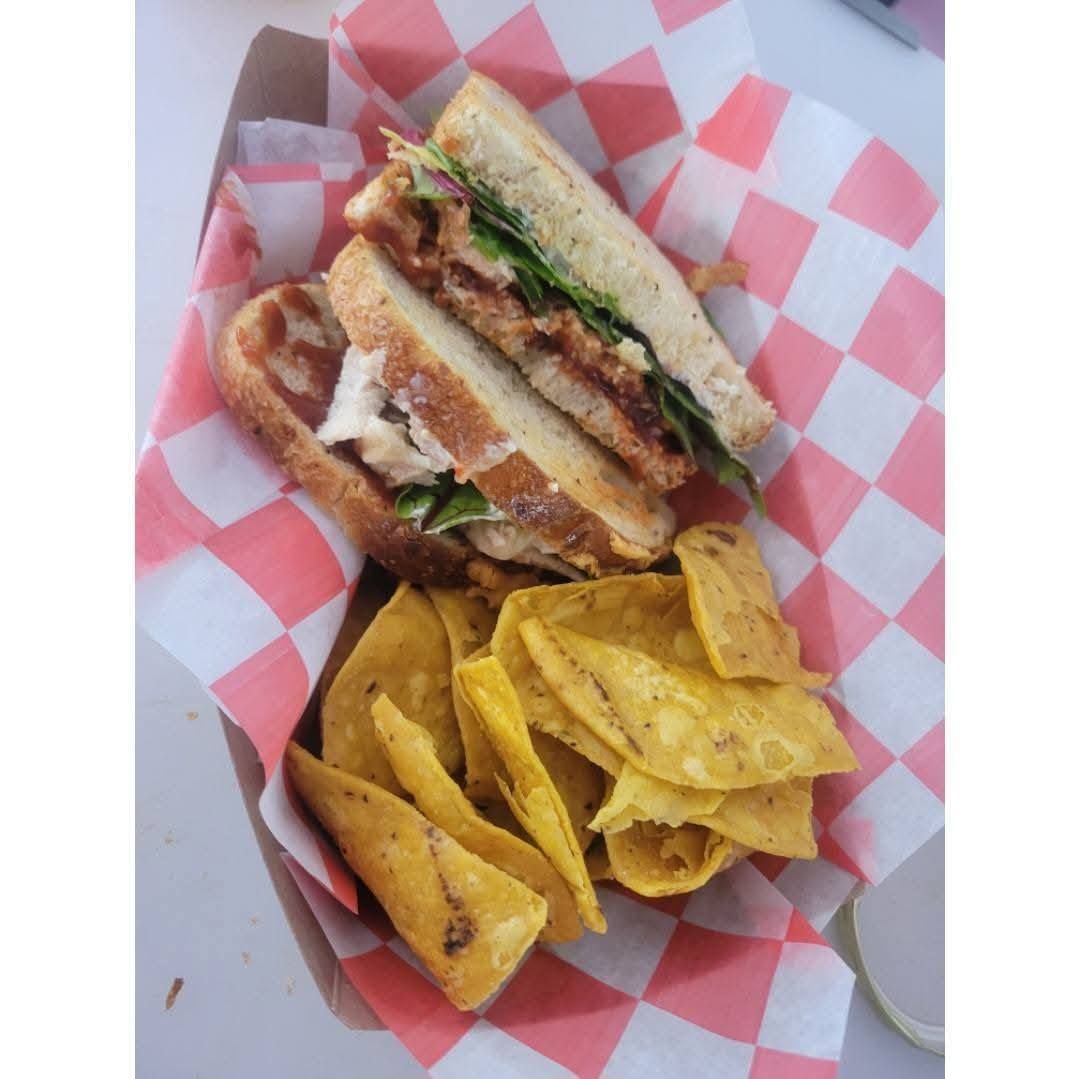Sandwich on checkered paper basket with yellow tortilla chips and fries, viewed from above