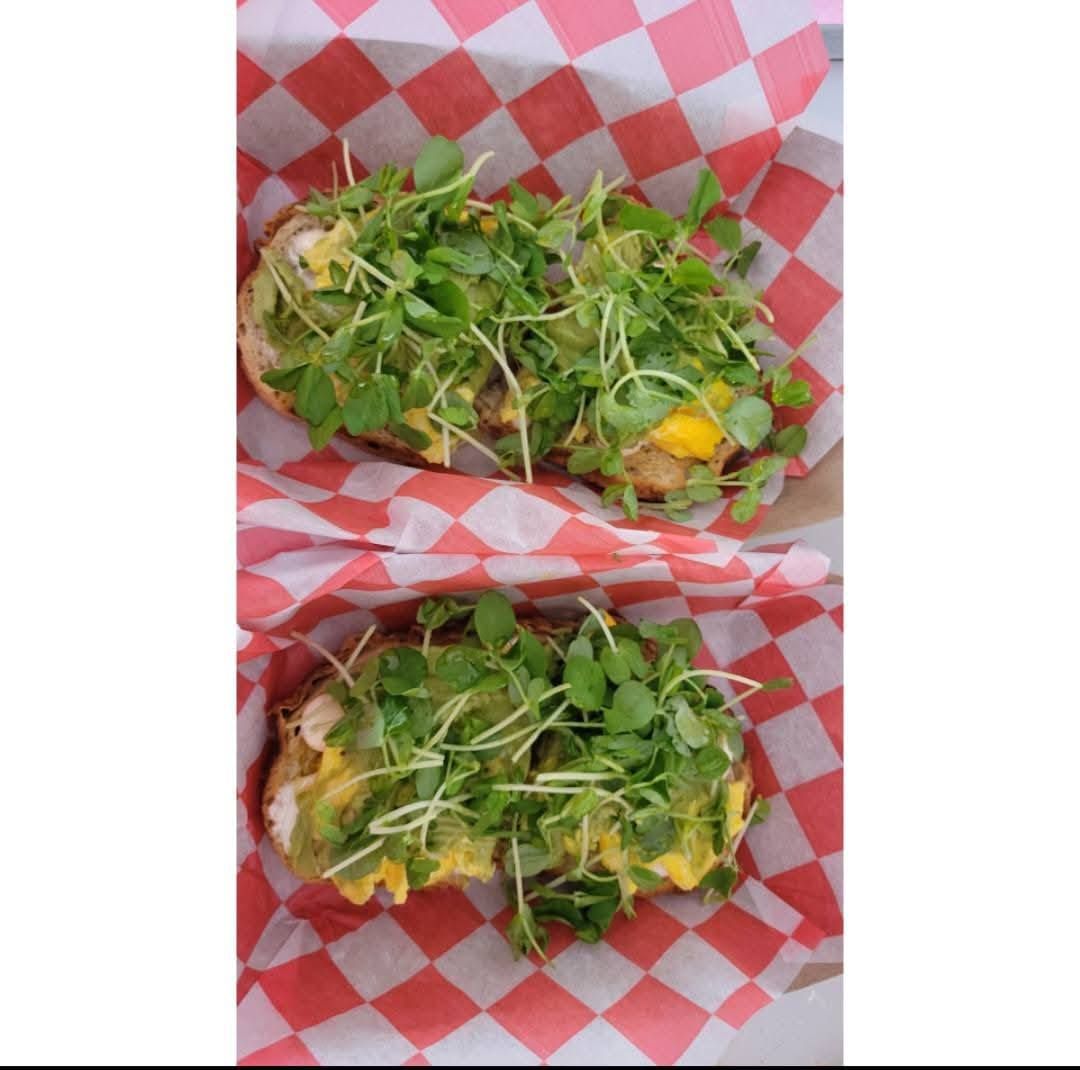 Two stuffed sandwiches topped with greens in red-and-white checkered paper trays