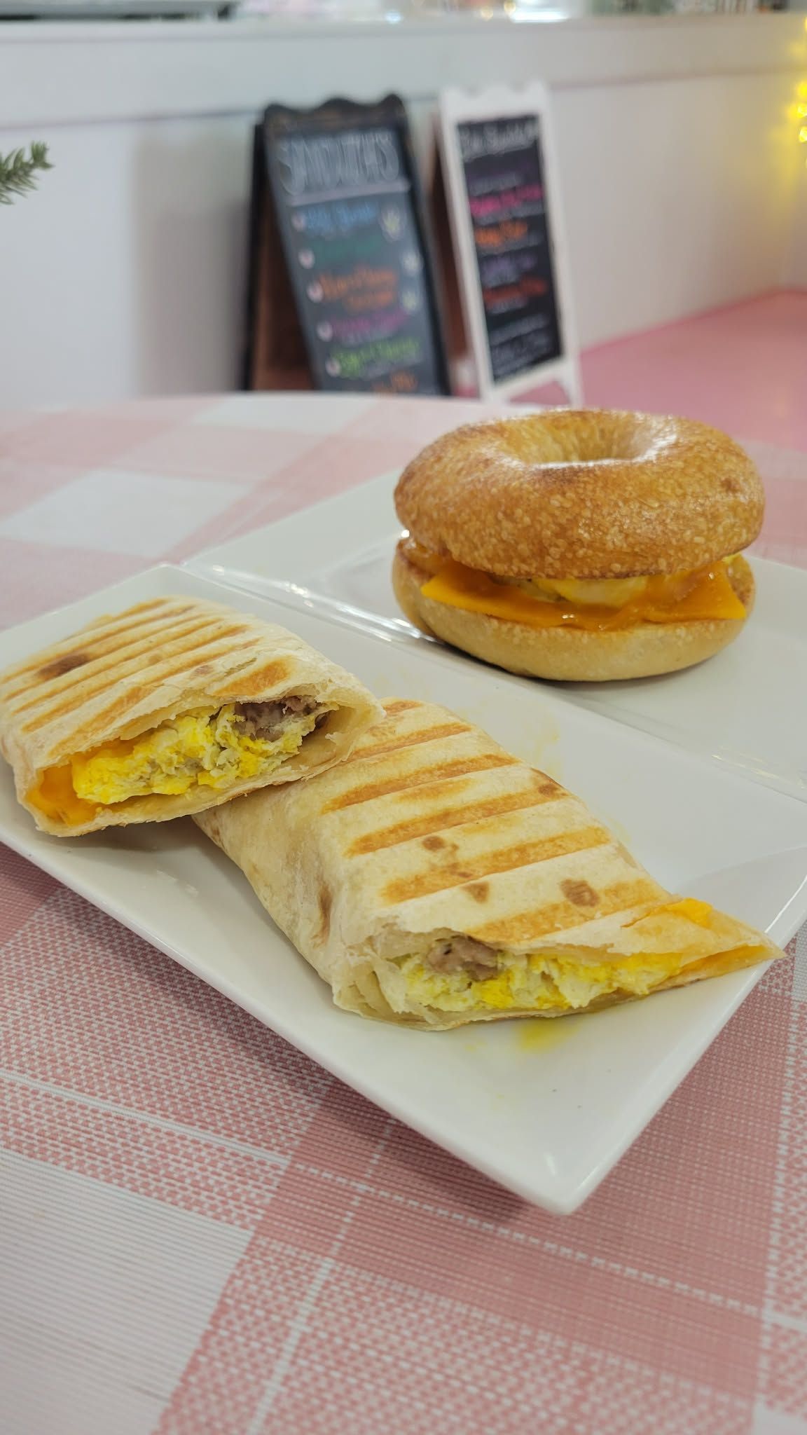 Wrap and a sesame bagel on a white plate over a pink tablecloth.