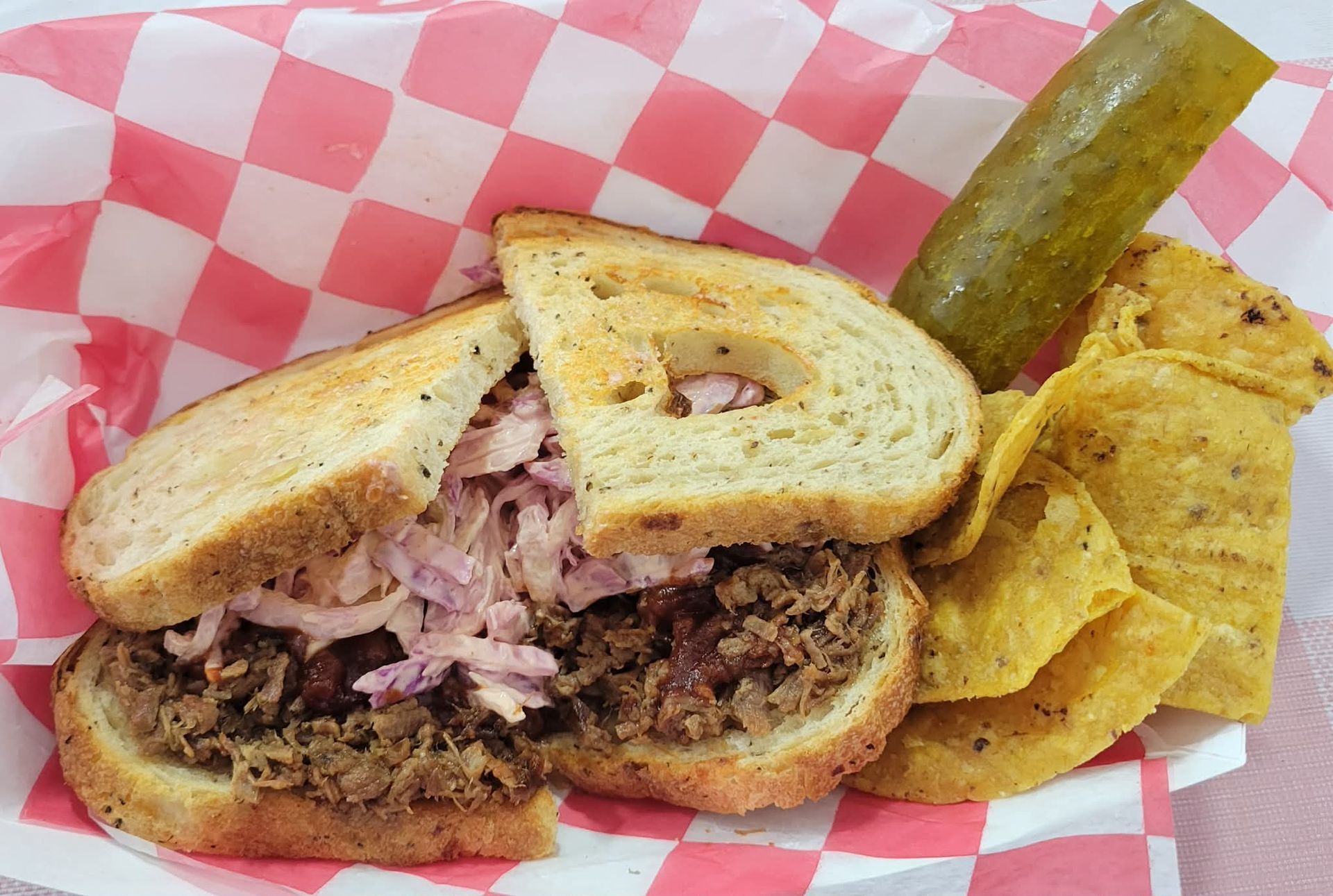 Turkey sandwich with chips and a pickle in a red-and-white paper-lined basket