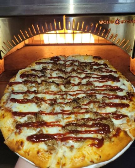 Cheese pizza with red sauce drizzled on a tray inside a lit wood-fired oven