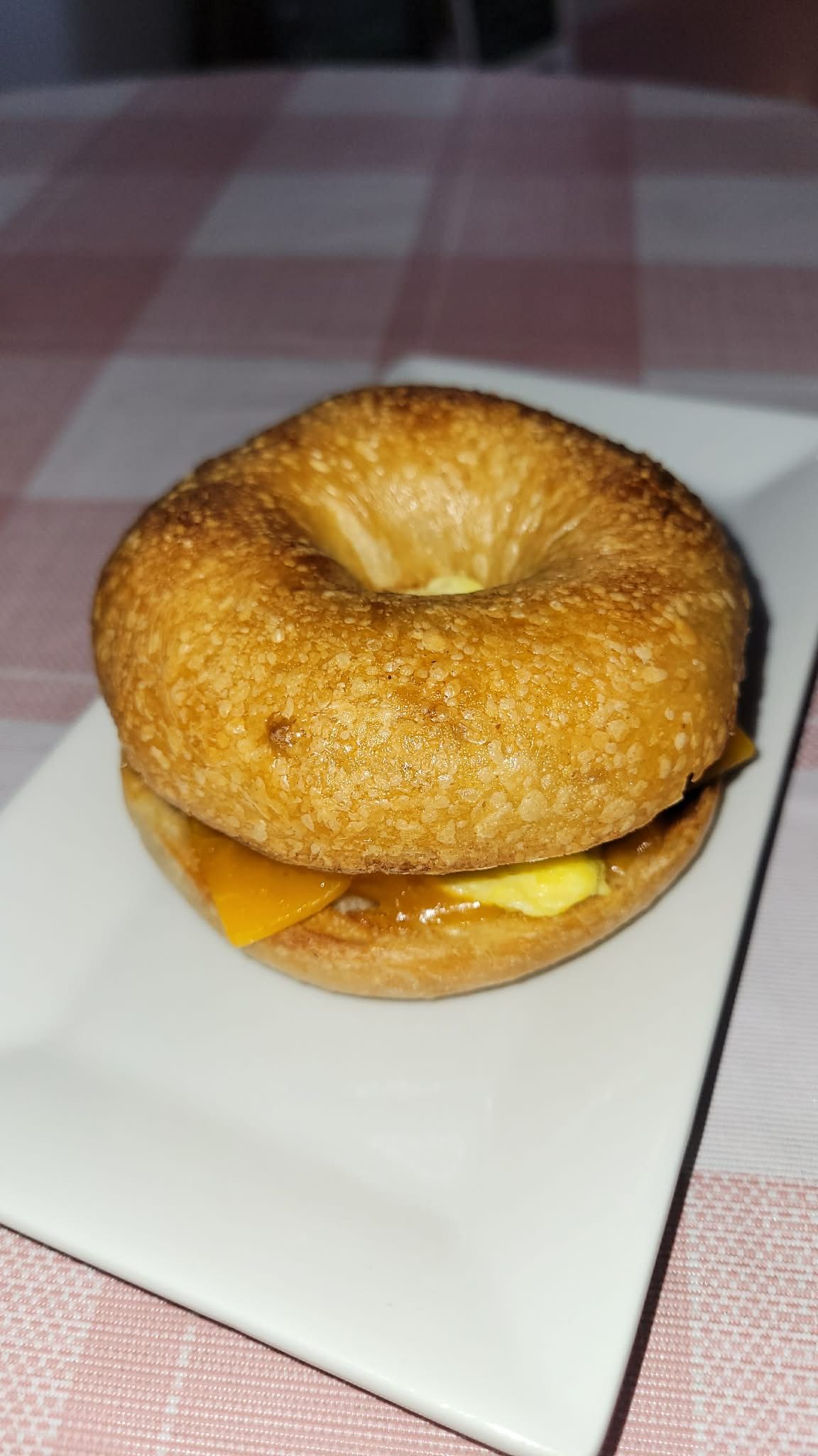 A plain bagel breakfast sandwich with melted cheese on a white plate