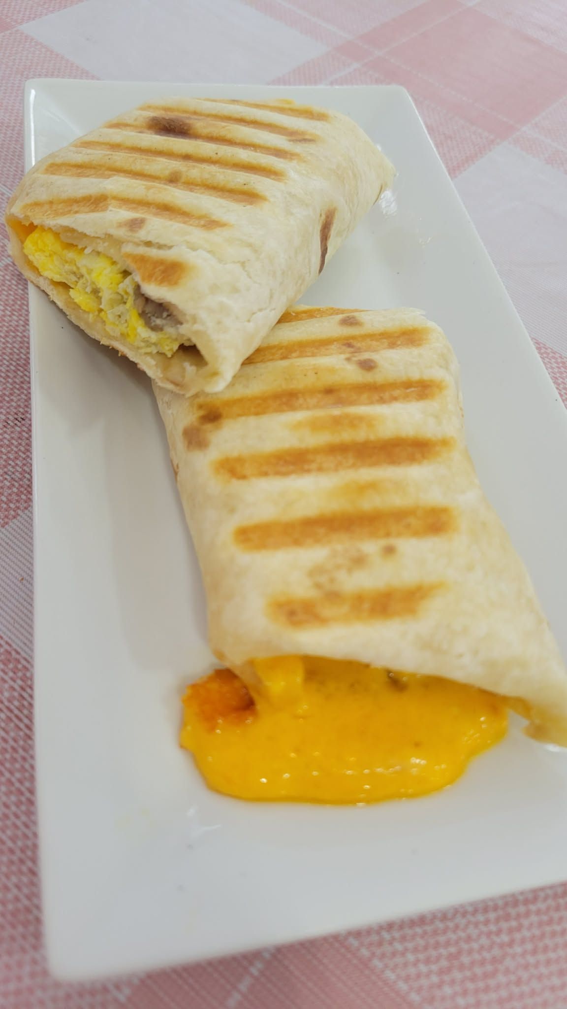 Grilled wrap sandwich on a white plate, cut open with melted yellow filling spilling out.