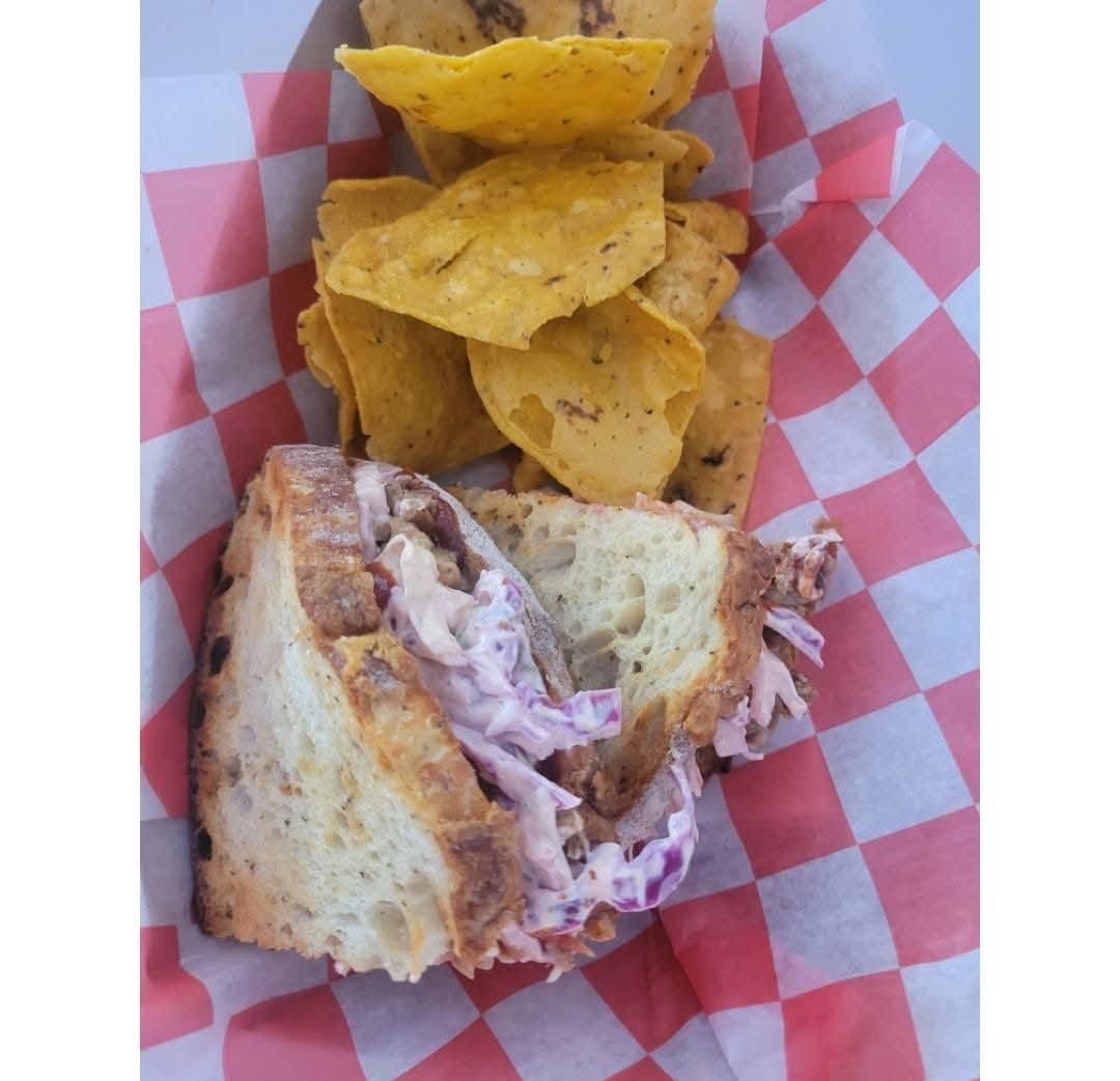 Sandwich halves with creamy filling and yellow tortilla chips in a red-and-white check paper basket.