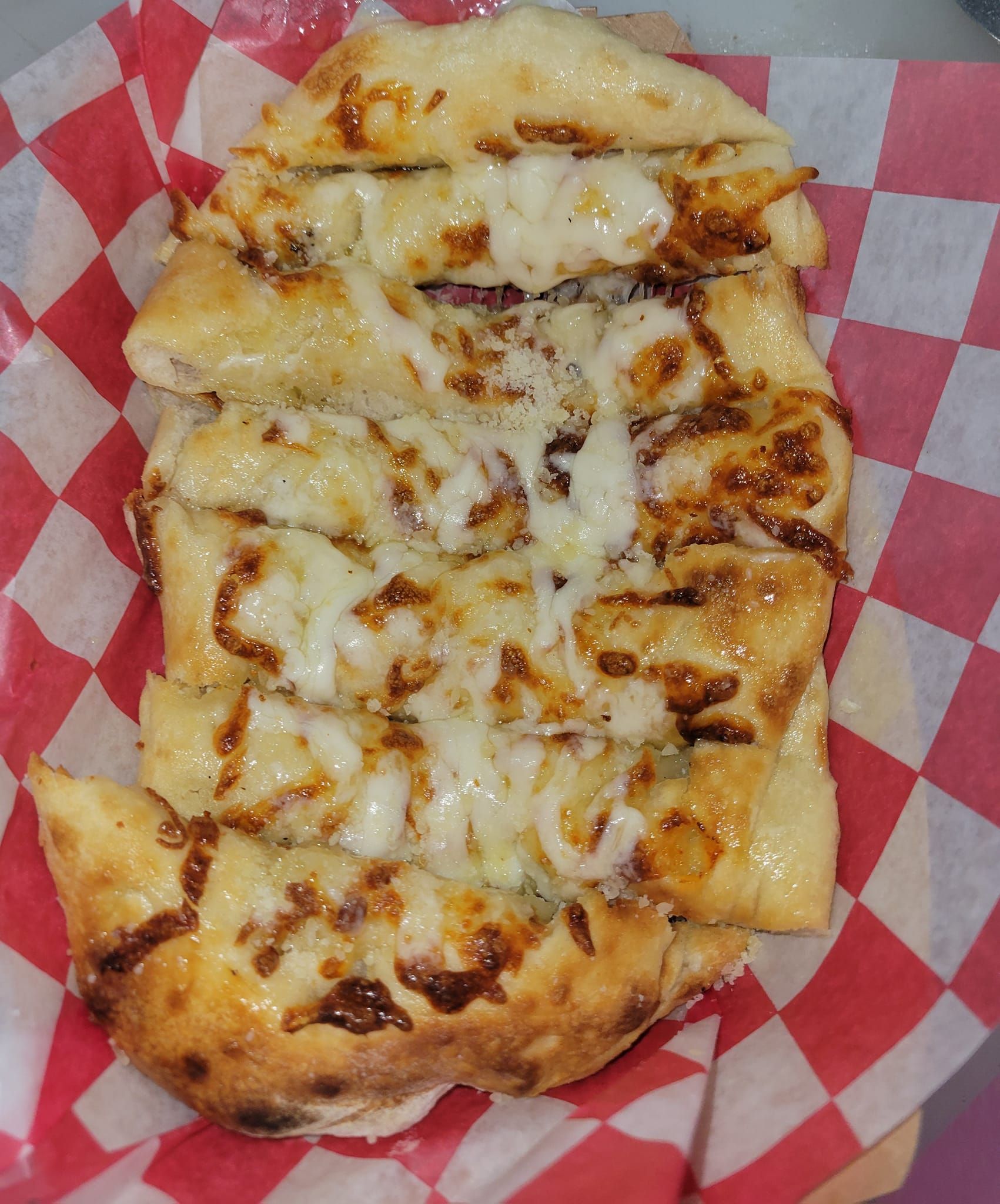 Cheesy pizza with browned crust on red-and-white checkered paper