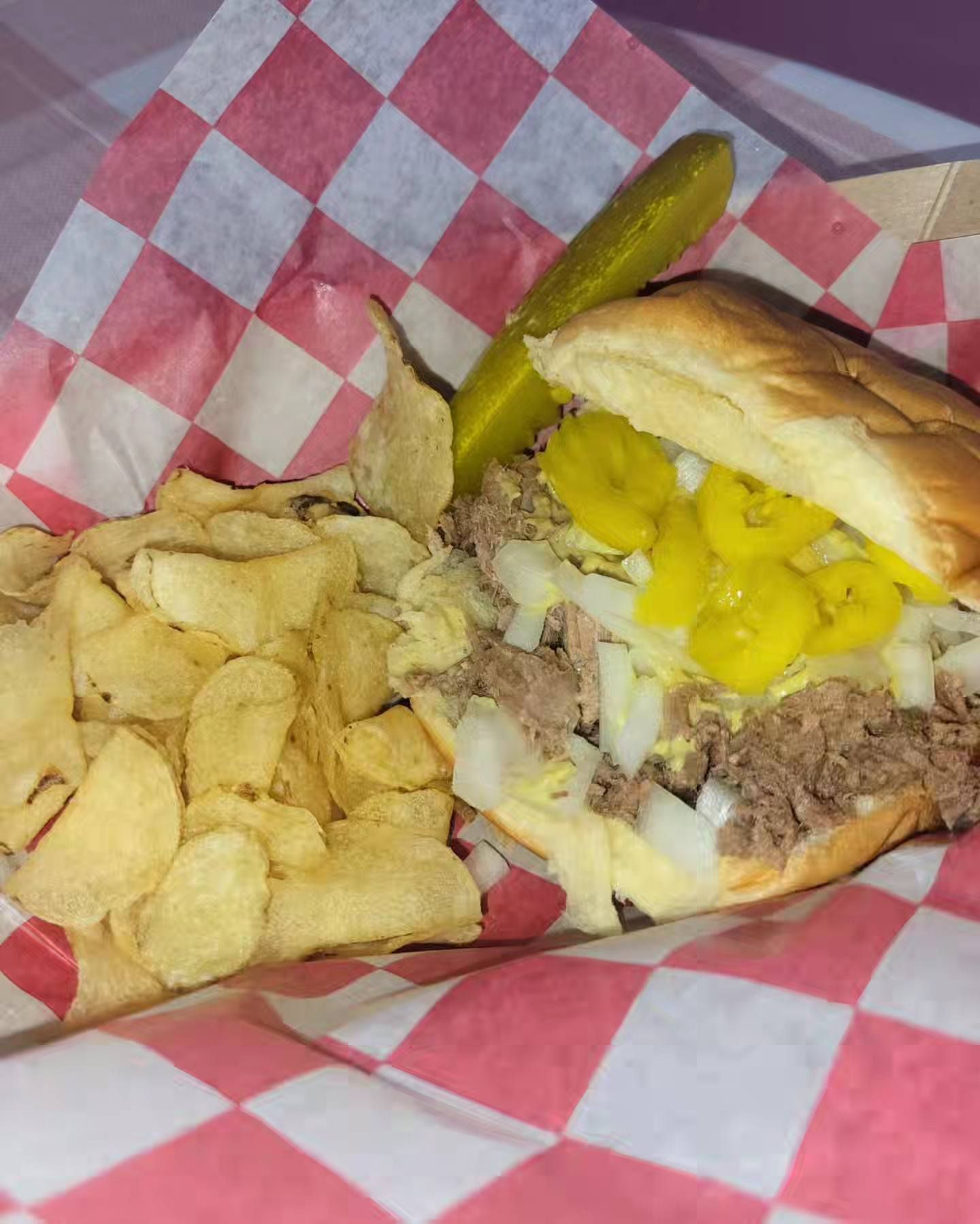 Burger with banana peppers and chips in red-and-white basket liner