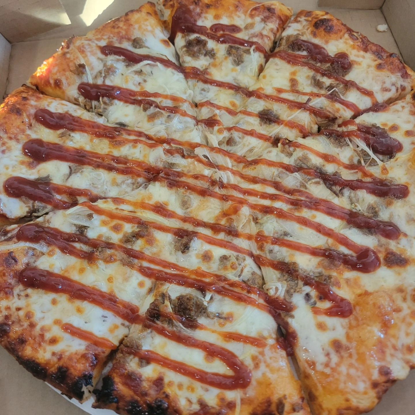 Close-up of a cheese pizza drizzled with ketchup and sliced into wedges in a box