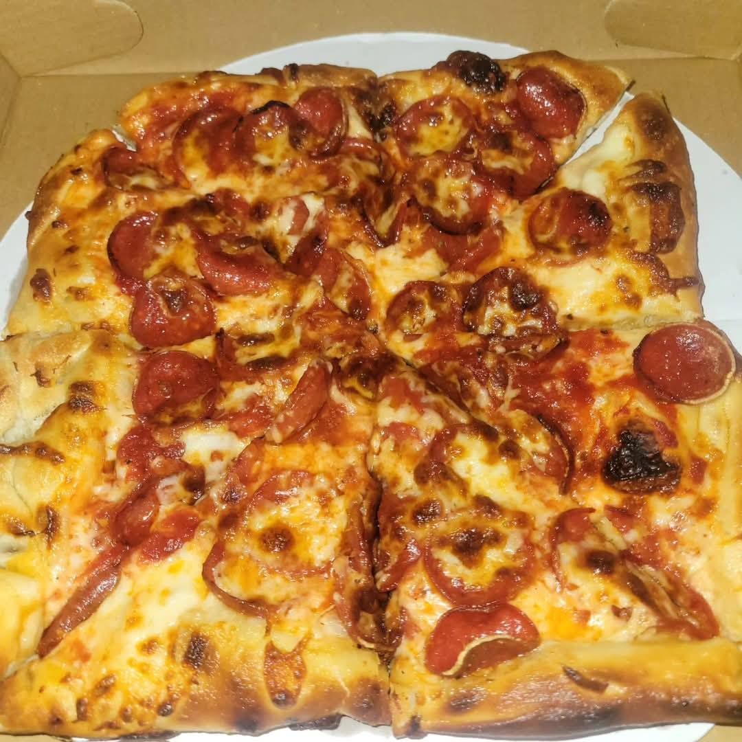 Square pepperoni pizza on a white plate, with melted cheese and browned crust.