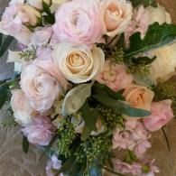 Soft bouquet of pale pink and cream roses with greenery, arranged tightly together.