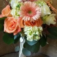 Bouquet of pink, peach, and white flowers with green leaves tied with a white ribbon