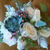White and pale blue floral bouquet with roses, berries, and greenery on a brown woven background