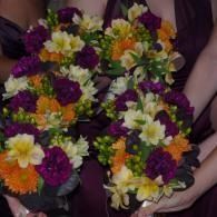 Two flower leis with purple, yellow, orange, and white blossoms held in hands