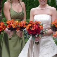Two people in formal dresses holding bright orange and red bouquets outdoors
