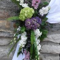 White and purple floral bouquet with greenery against a stone wall and draped white fabric