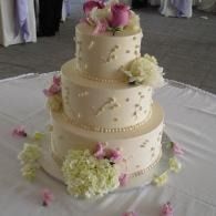 Three-tier white wedding cake with pink and cream flowers on a table