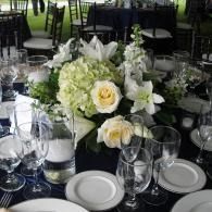Elegant banquet table with white floral centerpiece, glassware, and white plates on dark tablecloth