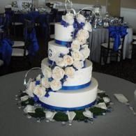 White tiered wedding cake with blue ribbon accents and white floral cascade on a decorated table