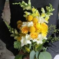 Bouquet of yellow and white flowers with green leaves, held against a dark background