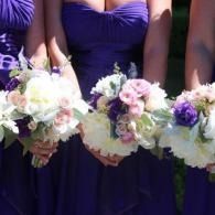 Bridesmaids in purple dresses holding white, pink, and lavender bouquets