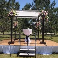 Outdoor wedding ceremony arch with floral arrangements and white drapery on a small wooden platform