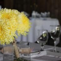 Yellow flowers in a vase on a set dining table with wine glasses and white tablecloth