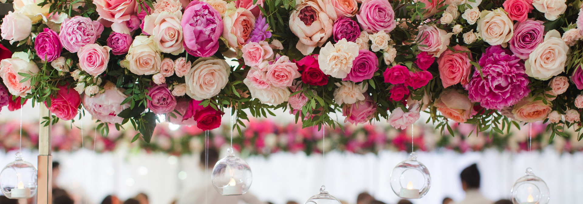 Pink and cream rose garland hanging across a softly blurred wedding-style backdrop