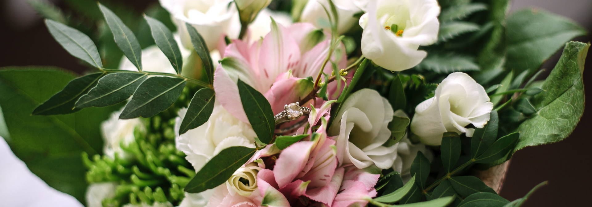 Pink and white roses with green leaves arranged in a bouquet, with a ring in the middle.