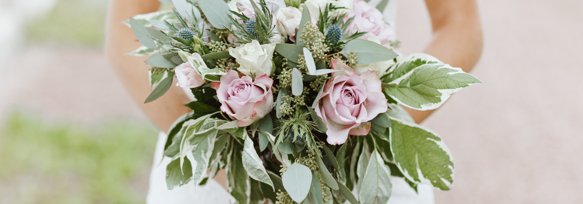 Bouquet of pale pink roses and greenery held in front of a white wedding dress