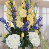 Yellow, purple, and white floral arrangement in a vase with hydrangeas and gladiolus.