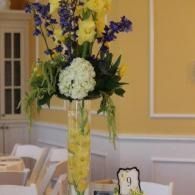 Tall yellow floral centerpiece with purple and white flowers on a banquet table indoors