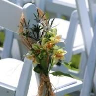 Flower bouquet tied to a white chair outdoors, with pale yellow and green blooms.