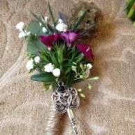 Small bouquet of green and white flowers with purple blooms and a silver key-shaped handle on tan fabric