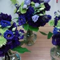 Purple and green flower bouquets in clear glass vases on a wooden table