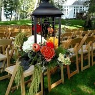 Outdoor wedding ceremony setup with rows of wooden chairs and a lantern floral centerpiece on the aisle