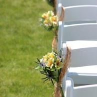 White chairs lined with small yellow-and-white floral bouquets on green grass outdoors