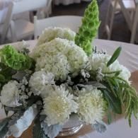 White floral bouquet with green foliage arranged in a glass vase on a table