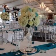 Elegant banquet hall with white floral centerpieces, teal table runners, and silver chairs